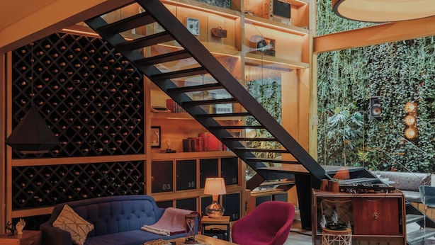 A modern interior with a staircase, a blue sofa, red ottomans, and a bookshelf.