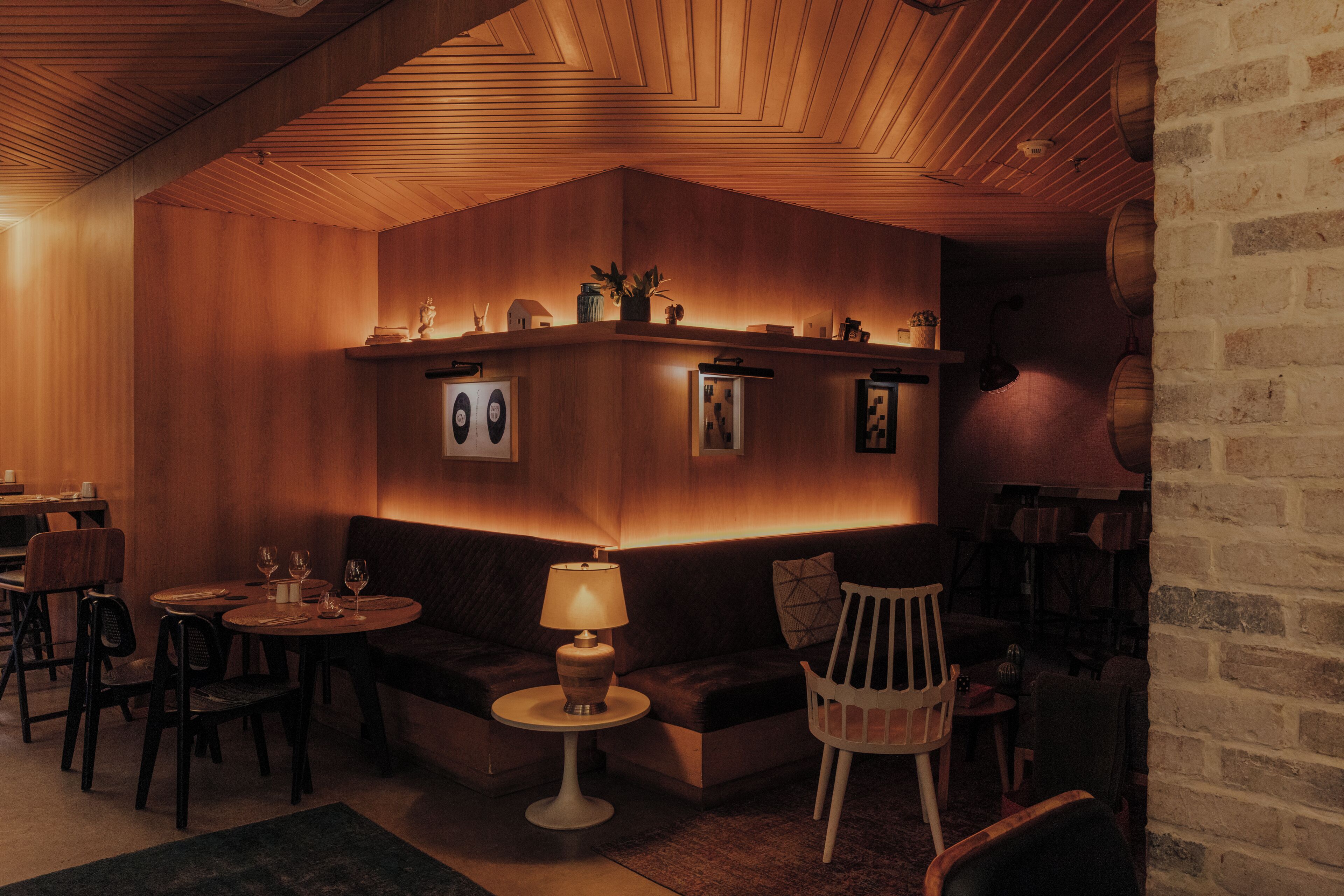 Un área de salón acogedora y tenuemente iluminada, con paredes de madera, asientos acolchados y una pequeña mesa redonda con una lámpara.