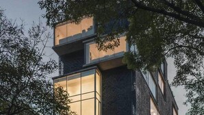 A modern multi-story building with large windows and balconies, surrounded by trees.