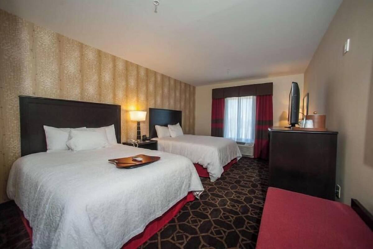 A hotel room with two beds, a desk, a lamp, a TV, and a red carpet.
