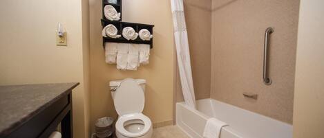 A bathroom with a toilet, a shelf with towels, a shower curtain, and a bathtub.