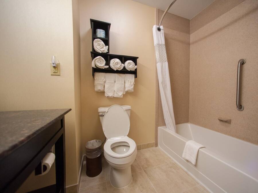 A bathroom with a toilet, a shelf with towels, a shower curtain, and a bathtub.