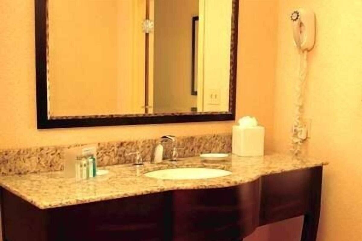 A bathroom with a granite countertop, a white sink, a mirror, and a hairdryer on the wall.