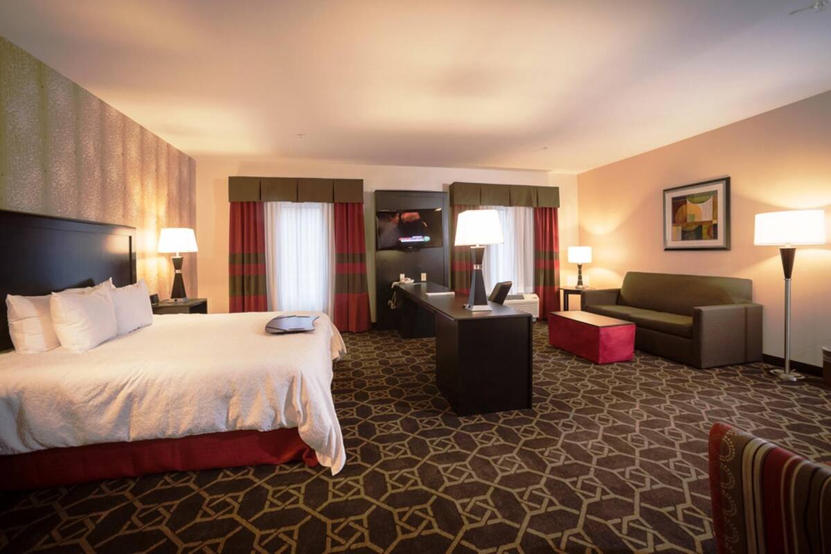 A hotel room with a bed, desk, chair, and sofa.