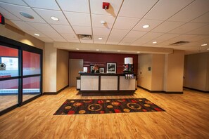 A hotel reception area with a wooden floor, a reception desk, a fire alarm, and a glass door with a sign.
