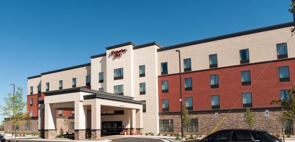 A modern hotel with a prominent 'Hampton Inn' sign, a covered entrance, and a multi-story building with a mix of beige and red exterior walls.