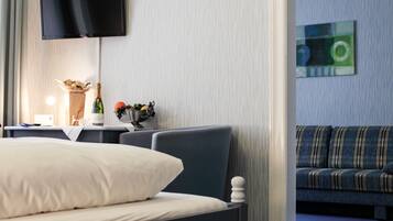 A hotel room with a bed, a desk with a lamp, a bottle of champagne, and a painting on the wall.