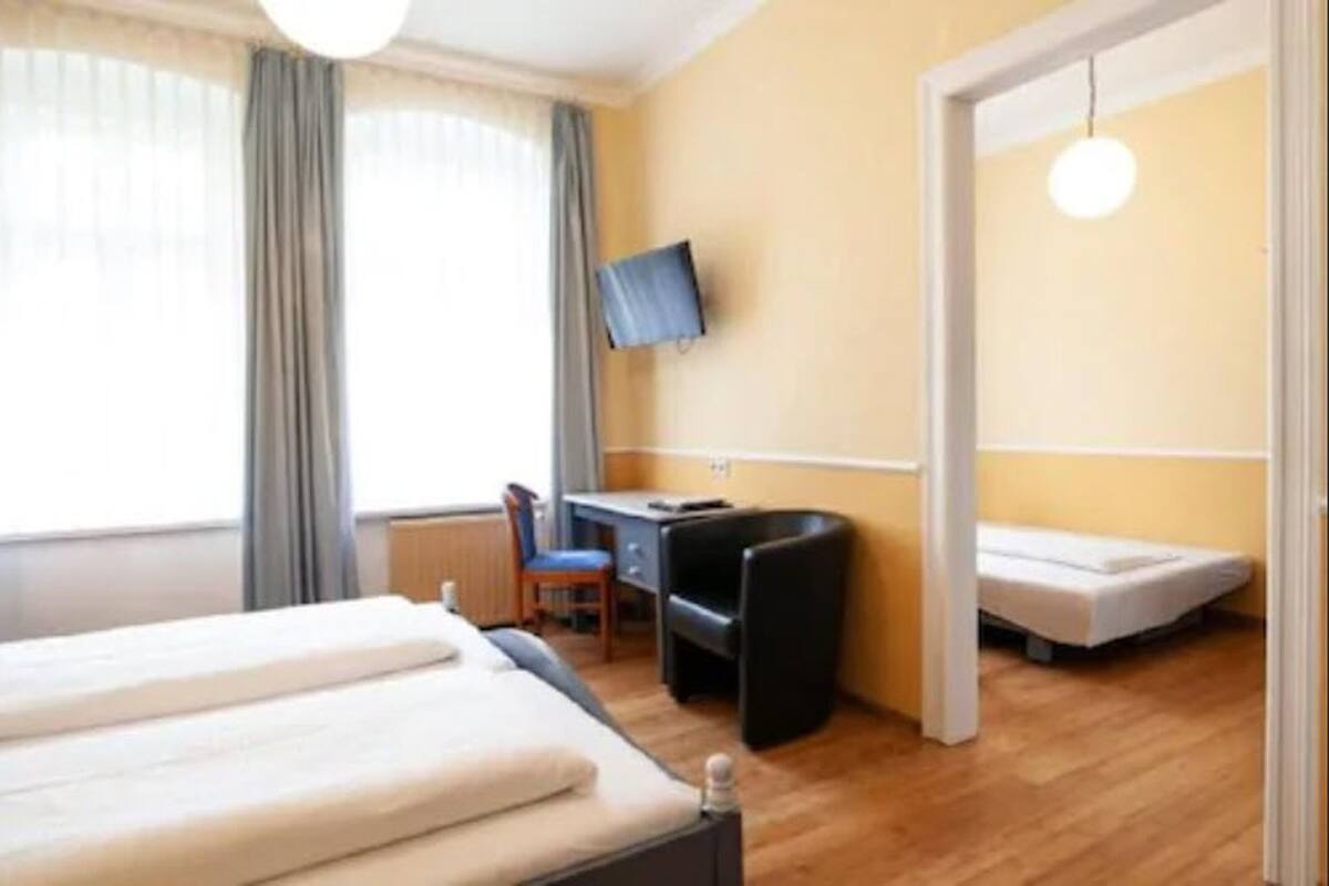 A hotel room with a bed, a desk, a chair, a TV, and a window with curtains.