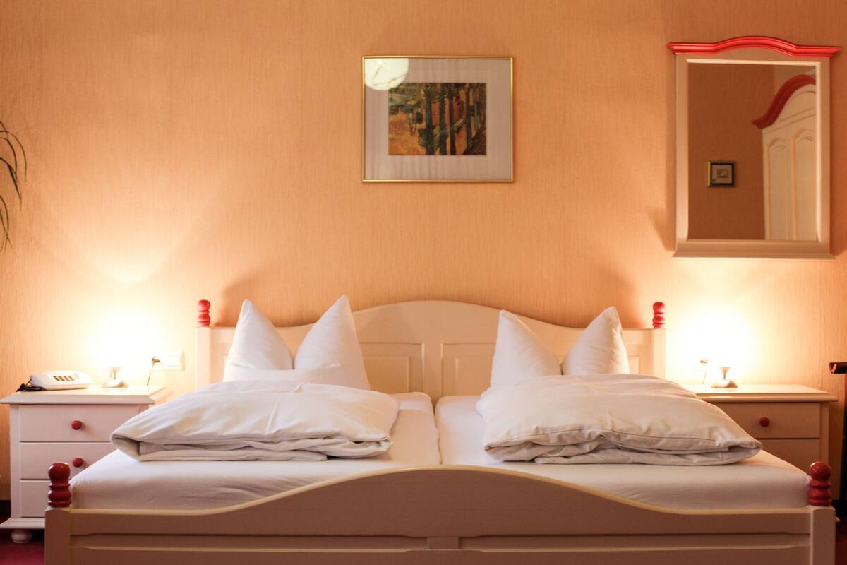 A neatly made bed with white linens and pillows, a bedside table with a lamp, and a framed picture on the wall.