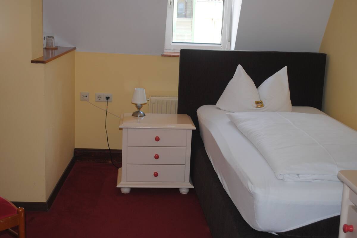 A bedroom with a bed, a nightstand, a lamp, and a window.