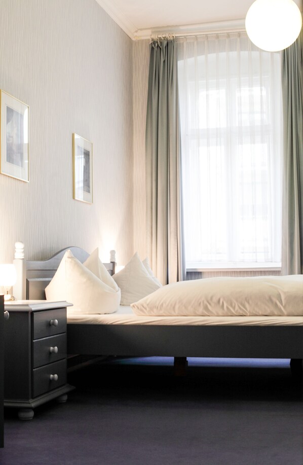 A bedroom with a bed, a nightstand, a dresser, and a window with curtains.