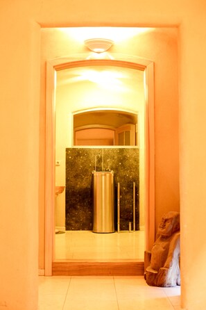 A bathroom with a marble wall, a stainless steel sink, and a statue.