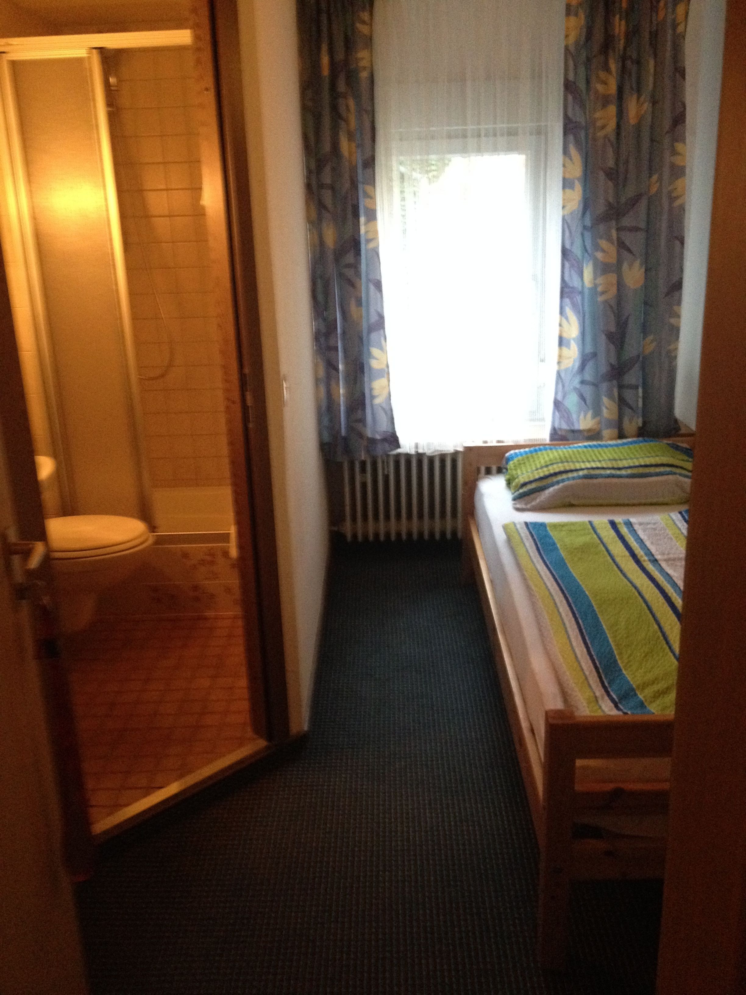 Una habitación de hotel pequeña y estrecha, con ducha, inodoro y una cama con manta a rayas.