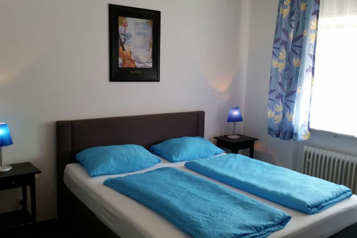 A bedroom with a bed, two bedside tables, a framed picture on the wall, and a window with curtains.