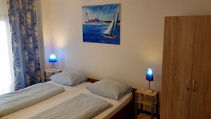 Un dormitorio con dos camas, un cuadro de un velero, un armario de madera y dos lámparas de noche.