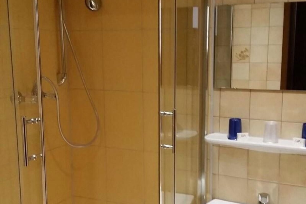 Un baño con ducha de vidrio, un lavabo blanco y pared de azulejos.