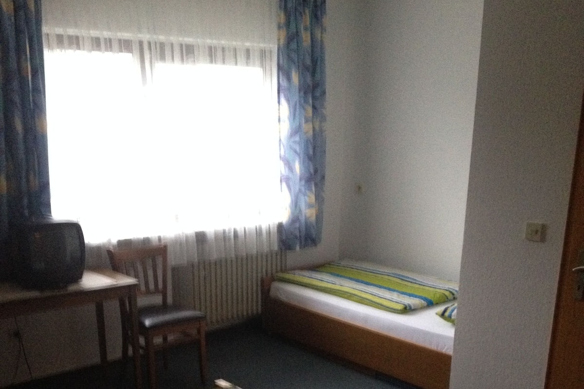 A room with two beds, a desk, a chair, and a radiator.