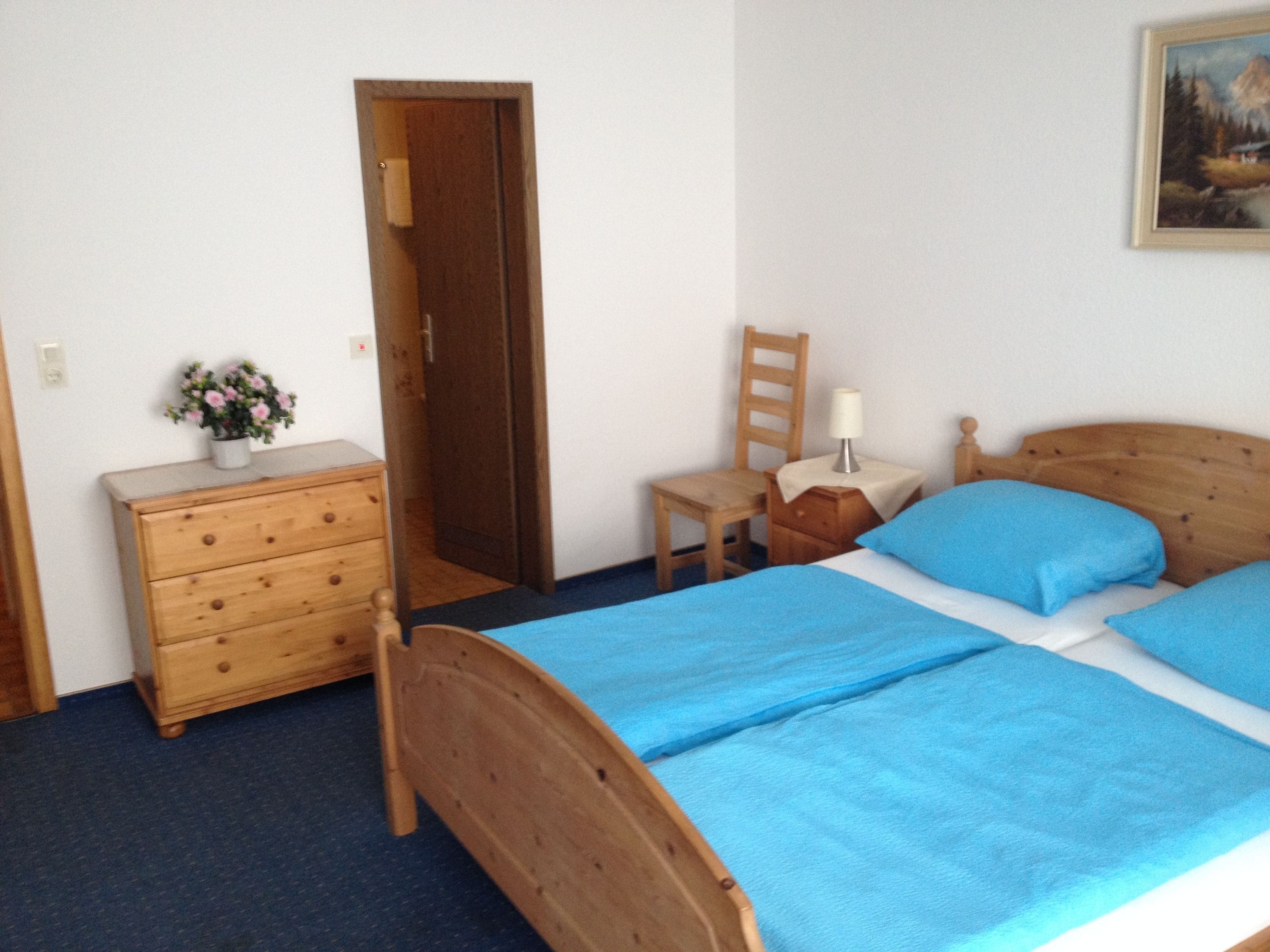 Ein Schlafzimmer mit einem hölzernen Bett, einer Kommode, einem Sessel, einem Nachttisch und einem Bild an der Wand.