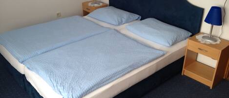 Una cama doble con cabecera azul y dos mesitas de noche, cada una con una lámpara.