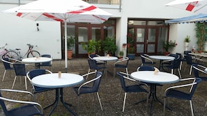 An outdoor seating area with round tables and chairs, umbrellas, and potted plants.