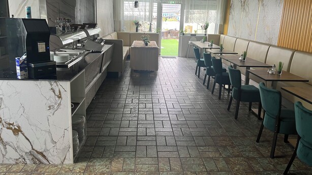 Un interior de restaurante moderno con paredes de mármol, una zona de cocina y un área de comedor con mesas y sillas.
