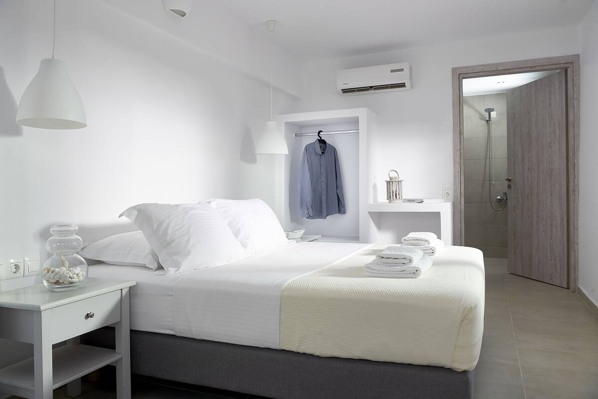 A modern hotel room with a bed, bedside table, hanging light, and a shower area.