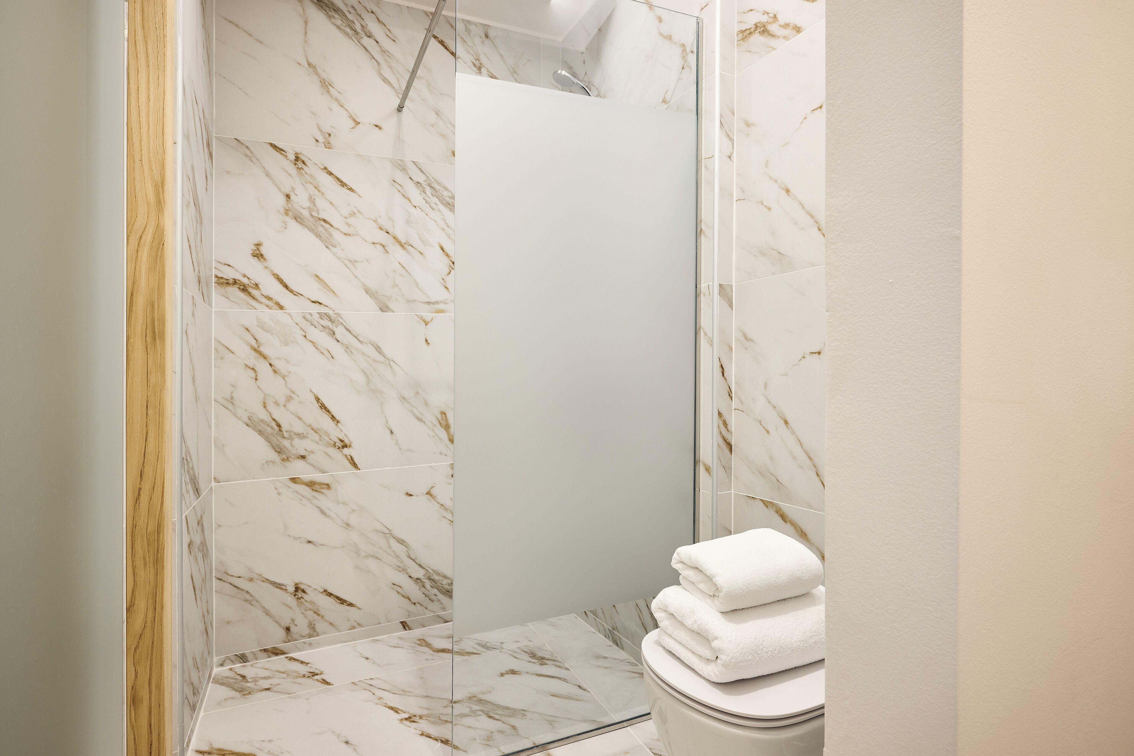 Une salle de bain dotée d’une douche à parois de verre, de carreaux de marbre et d’une pile de serviettes blanches.