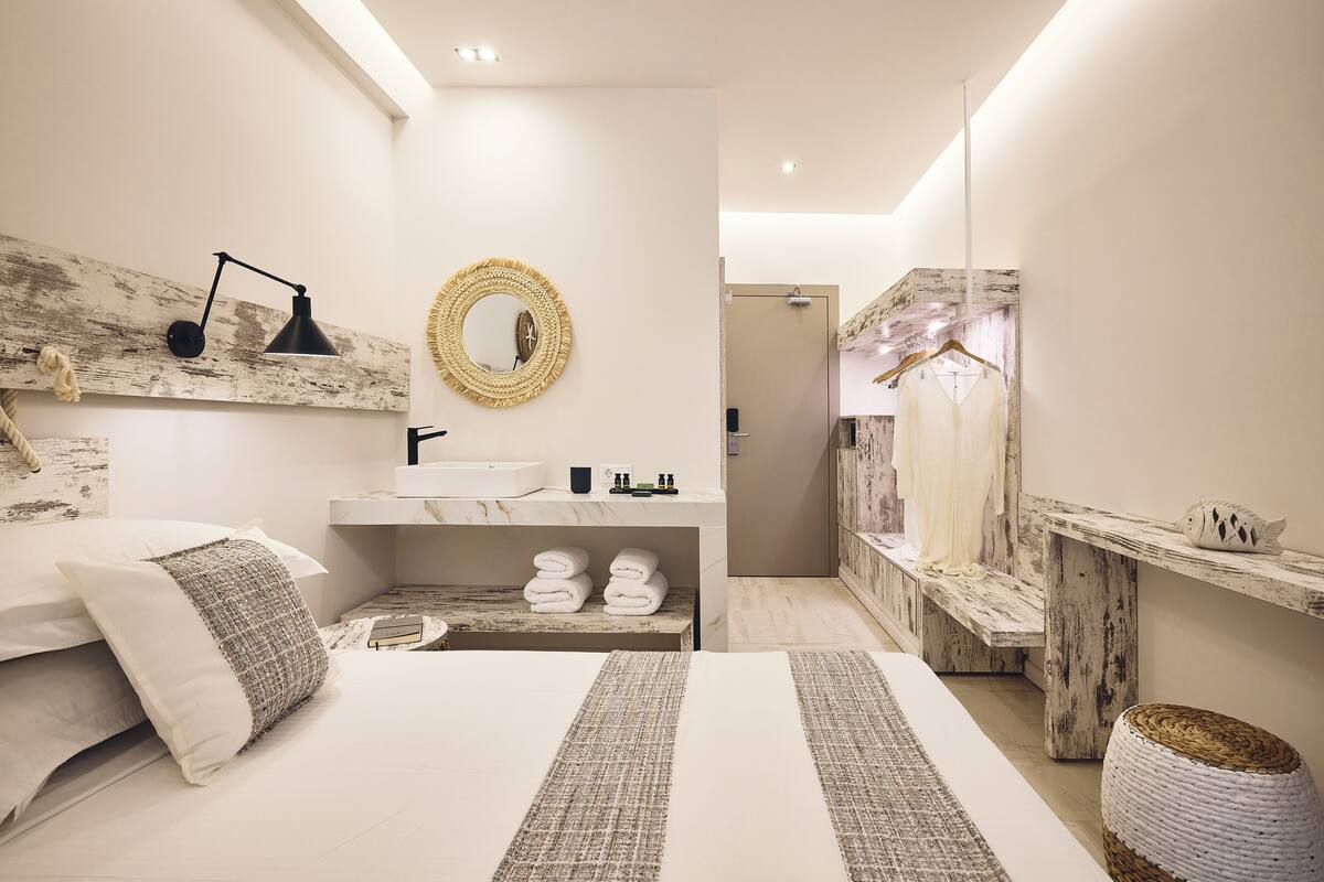 A modern bedroom with a large bed, bedside tables, a mirror, and a bathroom visible in the background.