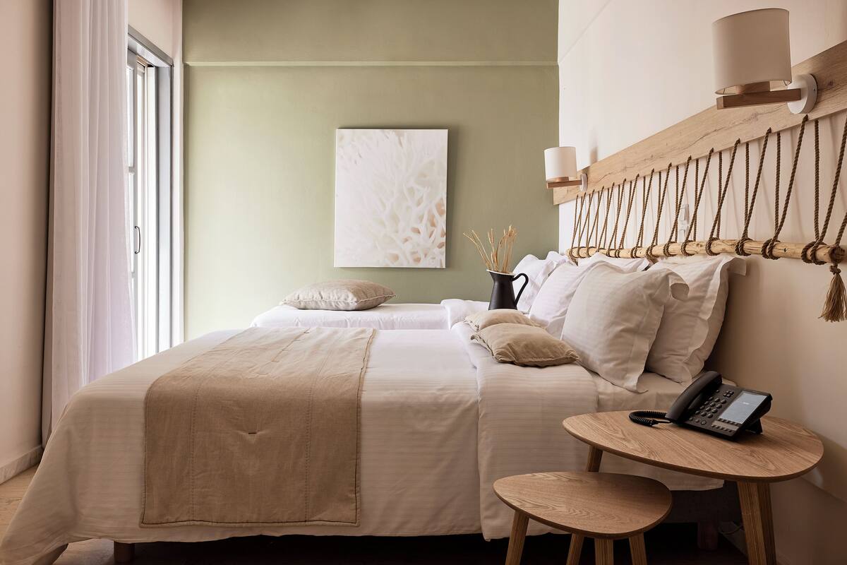 A bedroom with two beds, a bedside table, a lamp, and a painting on the wall.