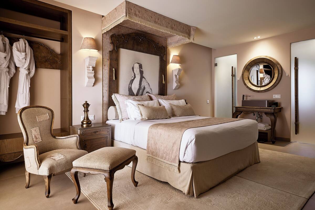 A bedroom with a large bed, a chair, a desk, a mirror, and two lamps.