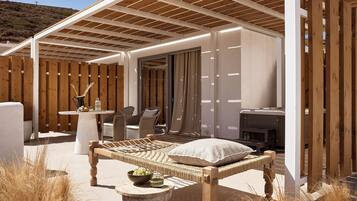 A covered outdoor seating area with a wooden bench, a table with a bowl of fruit, and wicker chairs.