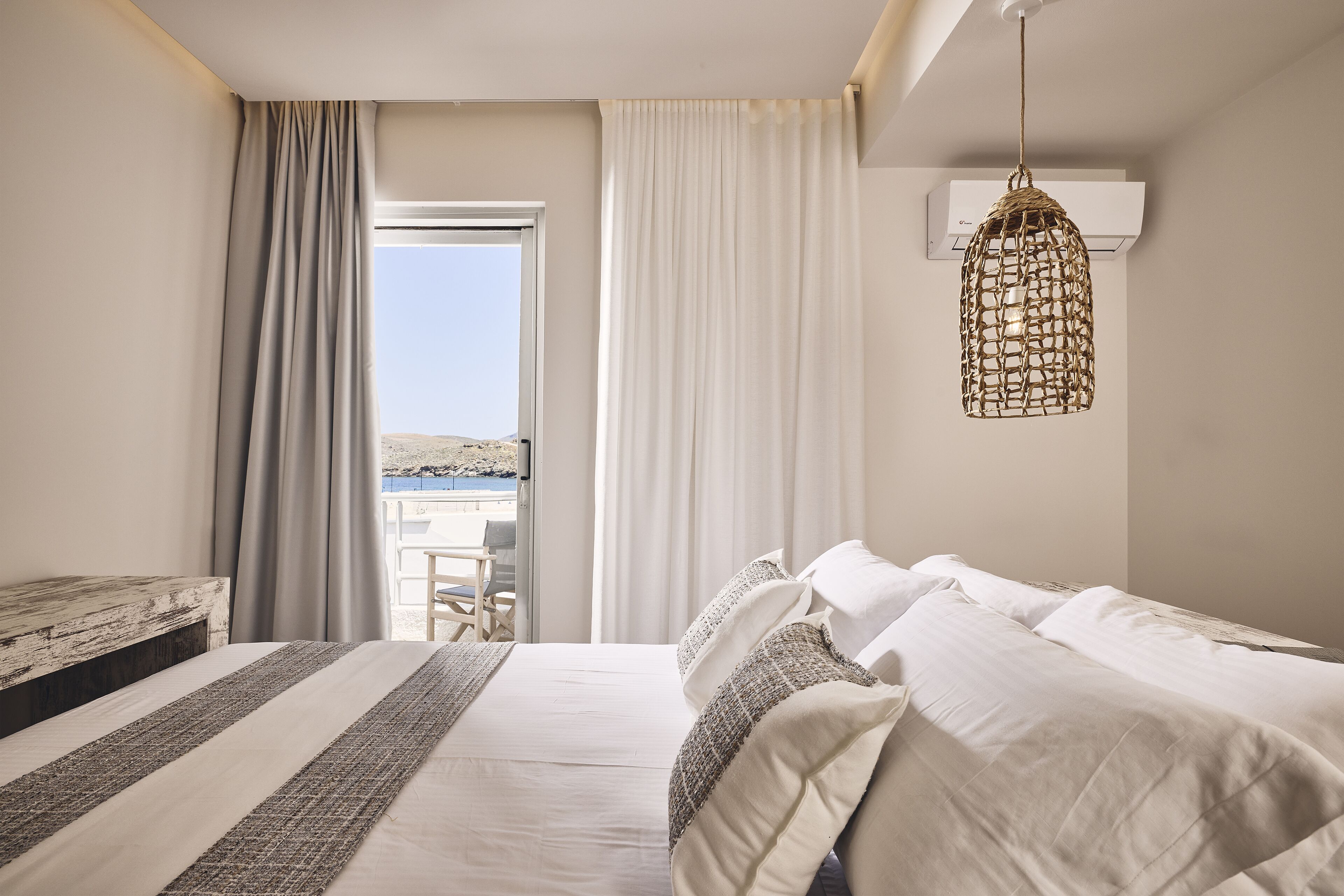Une chambre à coucher avec un lit, des rideaux, un luminaire suspendu et une vue sur l’extérieur.