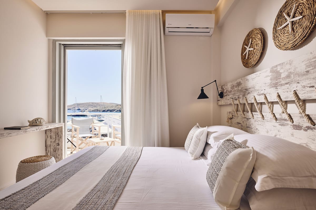 A hotel room with a bed, a view of the sea, a window with curtains, and a wall-mounted air conditioner.