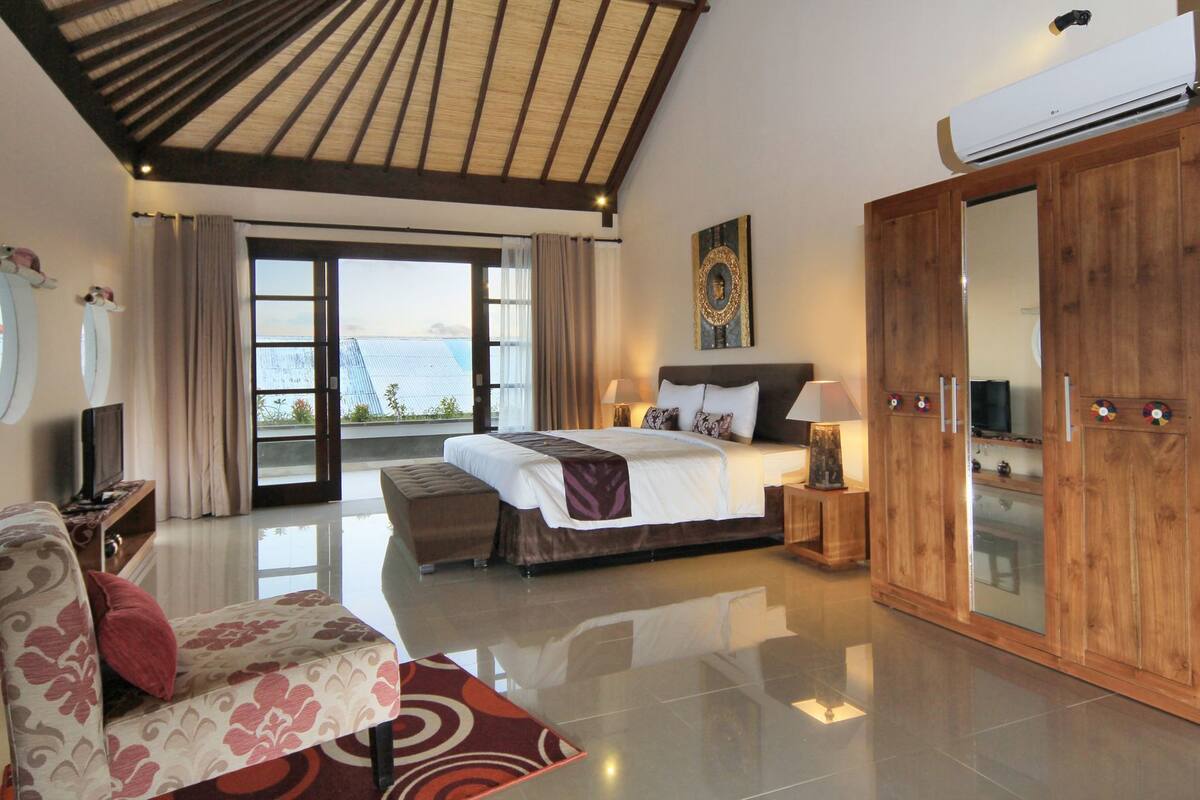 A spacious bedroom with a large bed, a wooden wardrobe, a sofa, and a television.