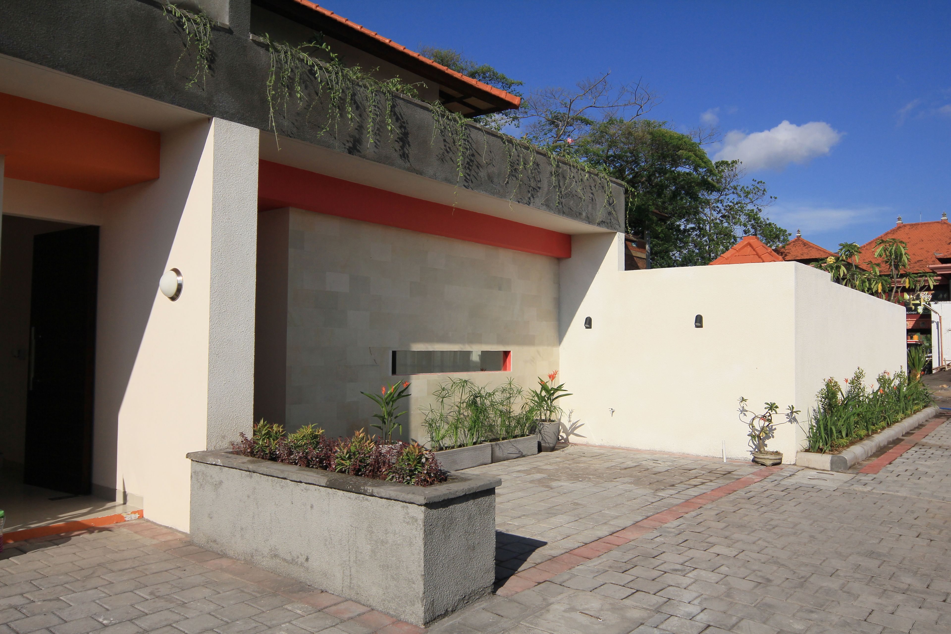 A modern building with a flat roof, concrete planter boxes with plants, and a paved walkway.