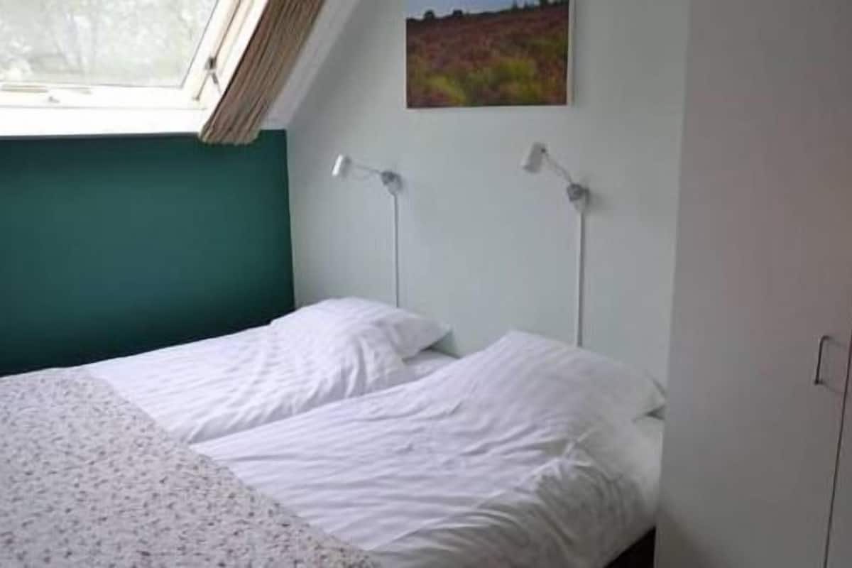 A bedroom with two single beds, a window, and a painting on the wall.