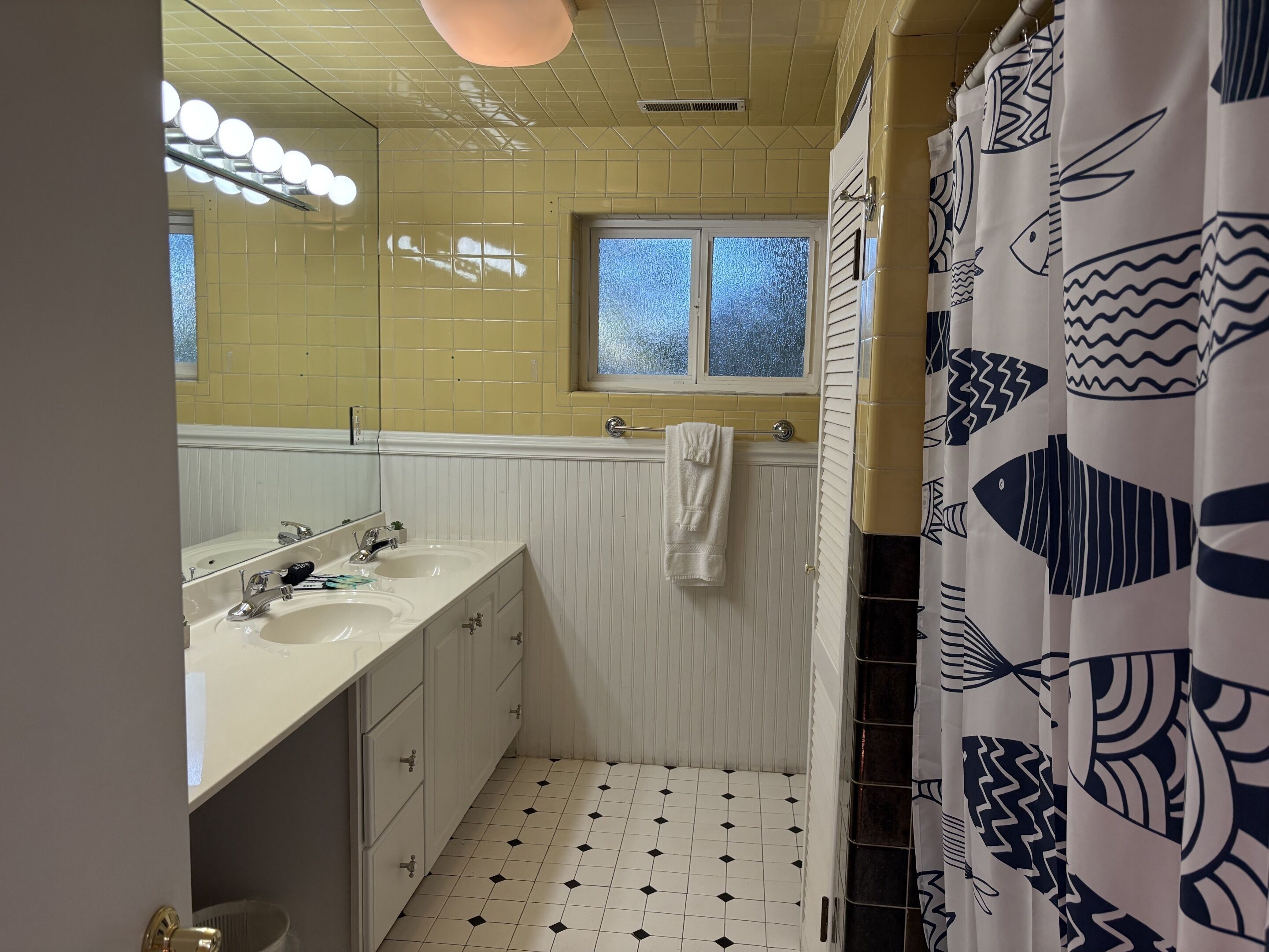 Un baño con dos lavamanos, una ventana y una cortina de ducha con motivos de peces.