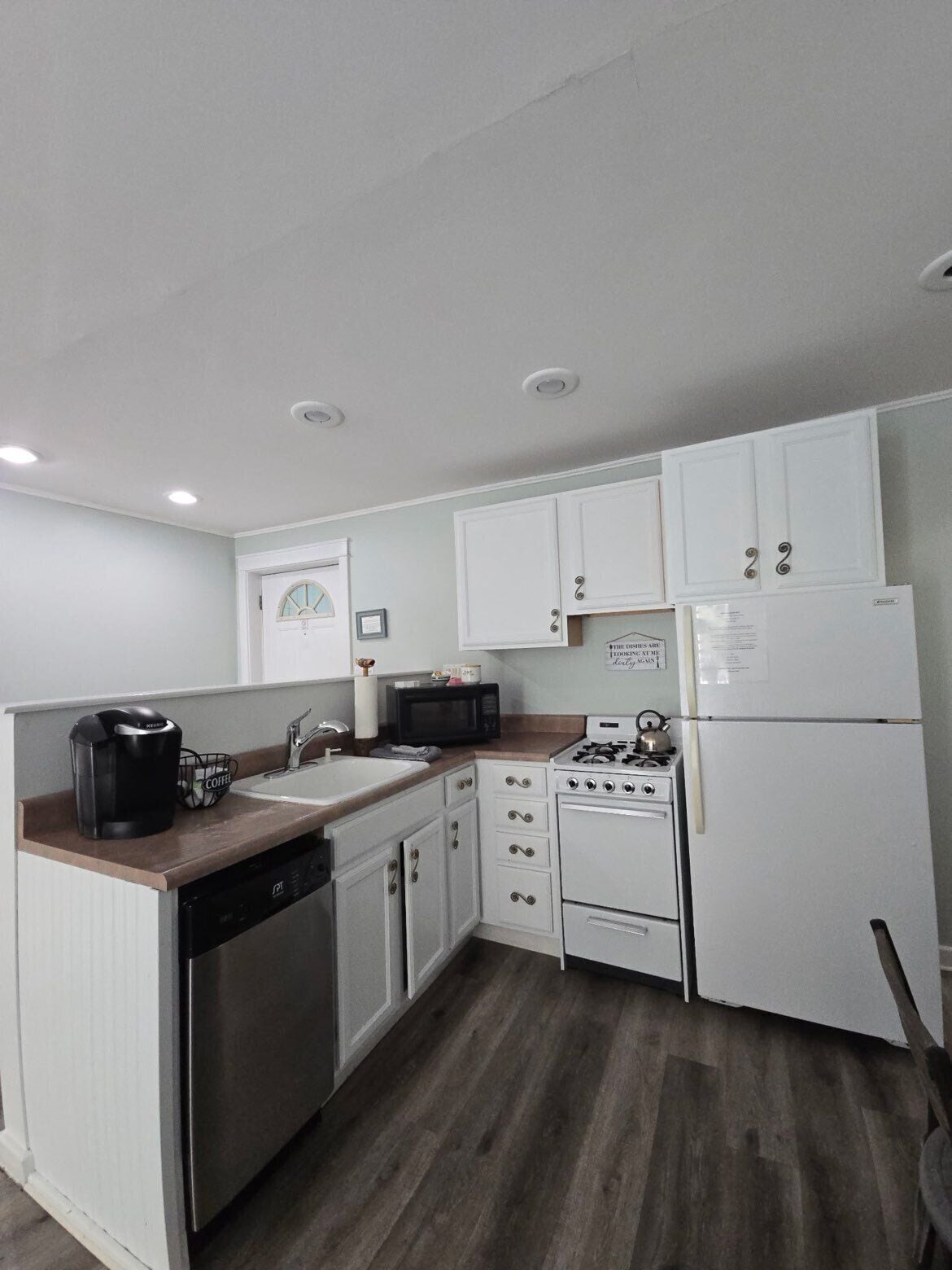 A compact kitchen with white cabinets, a microwave, a coffee maker, a dishwasher, and a stove.