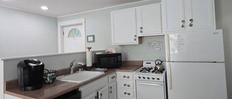 A compact kitchen with white cabinets, a microwave, a coffee maker, a dishwasher, and a stove.