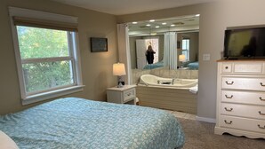 A bedroom with a bed, a vanity with a mirror, a bathtub, and a television. - New Buffalo Inn (New Buffalo)