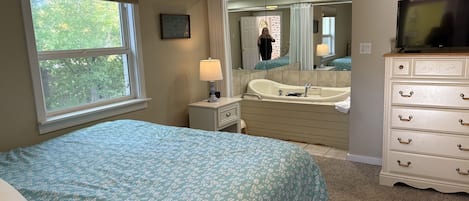 Un dormitorio con cama, tocador con espejo, bañera y televisor.
