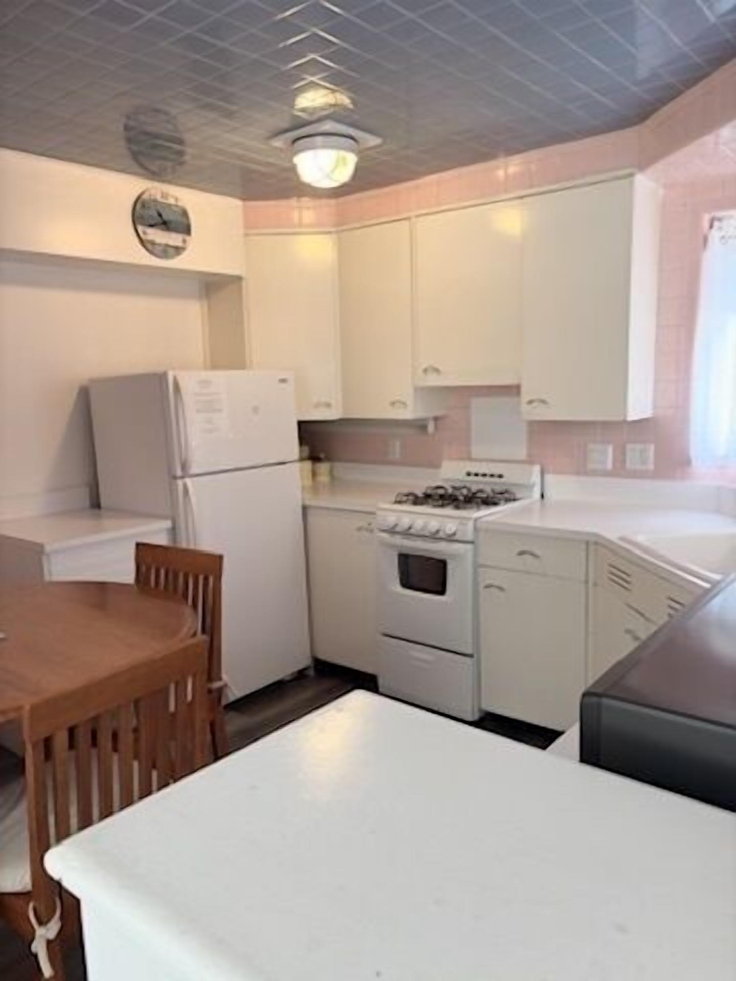 A compact kitchen with white cabinets, a refrigerator, a stove, and a dining table with chairs.