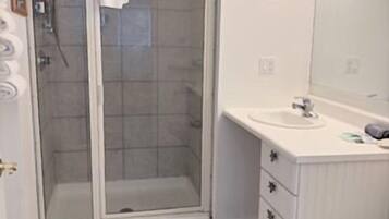A bathroom with a glass-enclosed shower, a sink with a mirror, and a toilet.