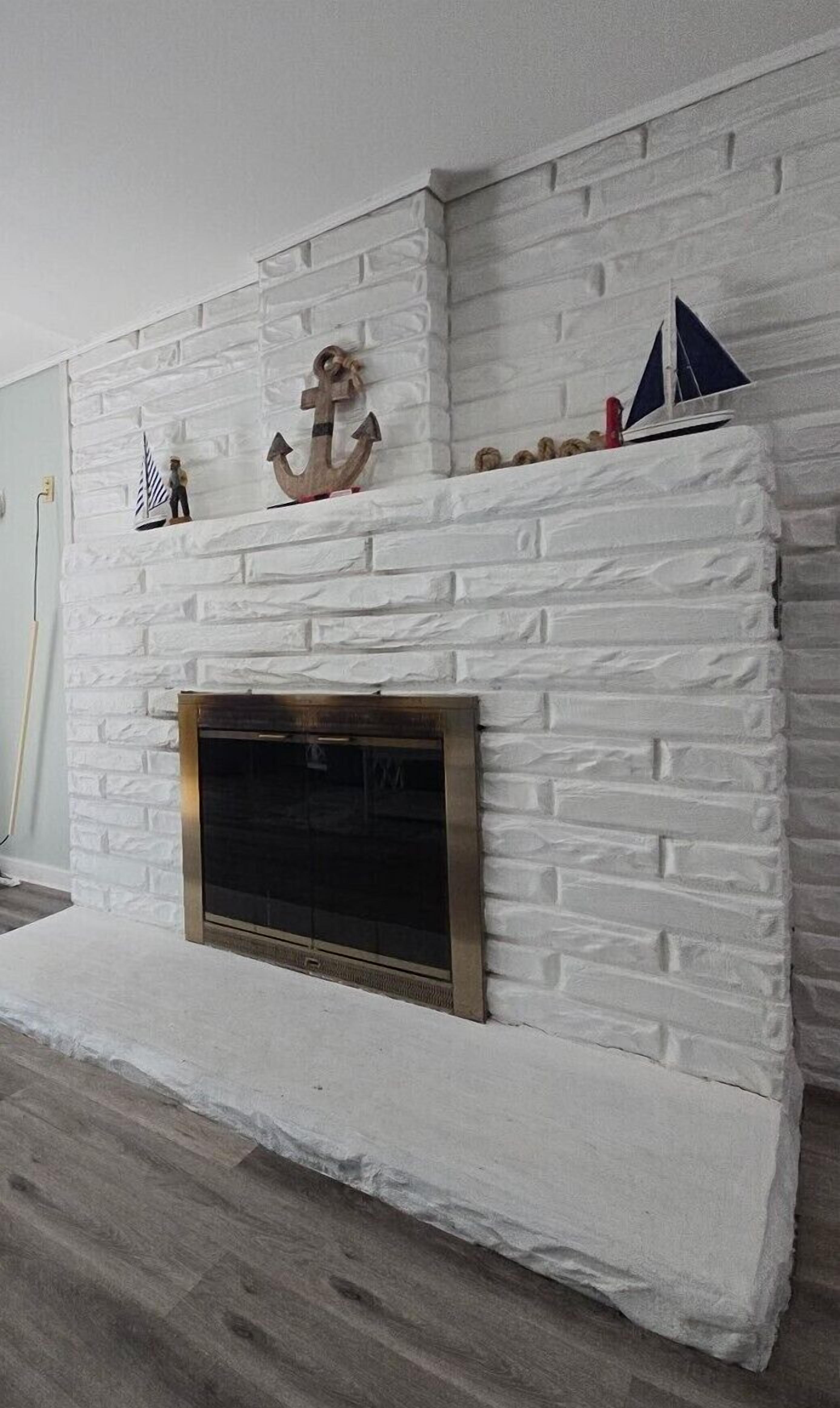 A white brick fireplace with a metal screen, a small shelf with decorative items, and a wooden floor.