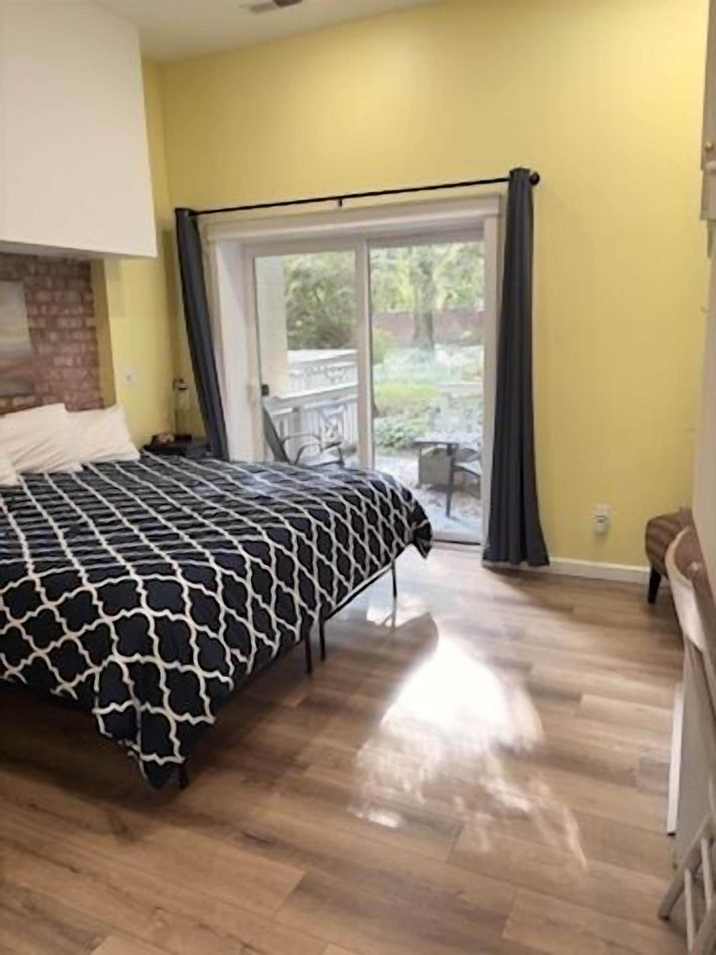 A bedroom with a bed, a brick wall, a sliding glass door to a balcony, and a wooden floor.