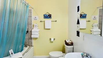 A bathroom with a yellow wall, a white sink, a white toilet, a blue shower curtain, and a mirror with lights.