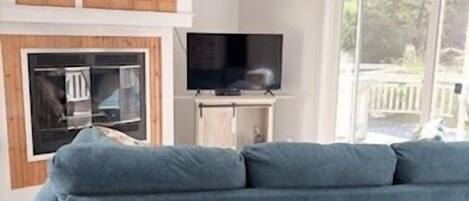A modern living room with a grey sofa, a ceiling fan, a flat-screen TV, and a fireplace.