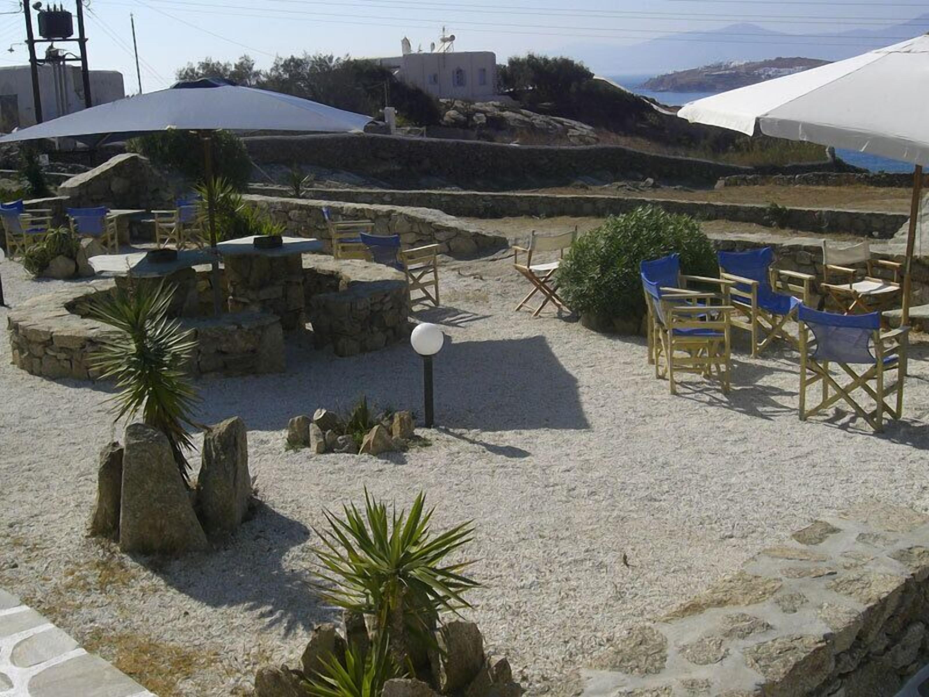 An outdoor seating area with stone tables and blue chairs, surrounded by rocks and plants.