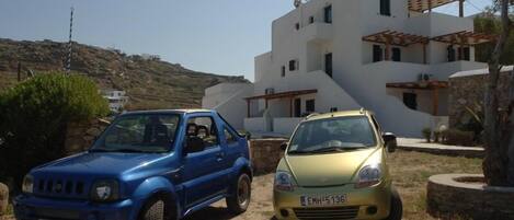 Dos autos estacionados frente a un moderno edificio blanco con base de piedra y una pérgola de madera.