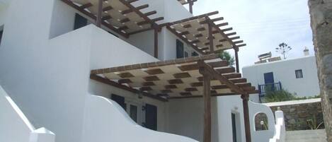 A white building with a wooden pergola on the second floor, a stone staircase, and a clear sky.